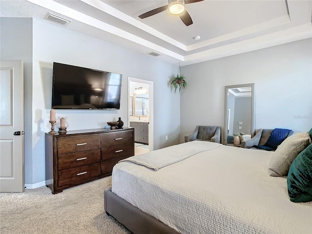 bedroom featuring a tray ceiling, connected bathroom, ceiling fan, and light carpet