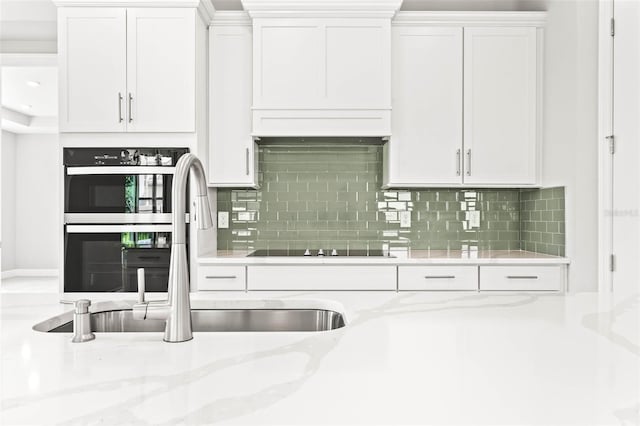 kitchen featuring light stone counters, sink, white cabinets, stainless steel double oven, and backsplash