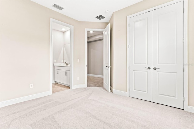 unfurnished bedroom featuring light carpet, sink, a closet, and ensuite bathroom