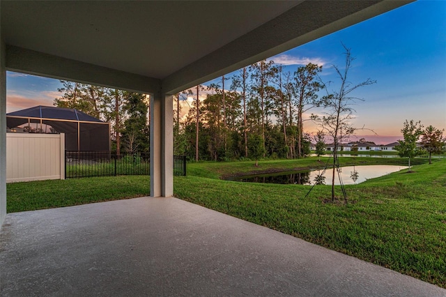 patio terrace at dusk featuring a lawn and a water view