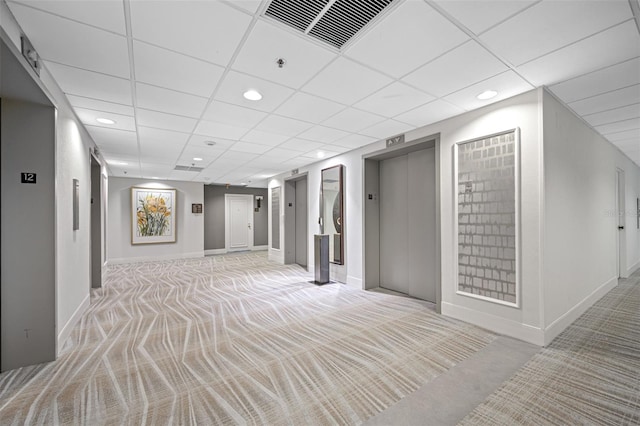 corridor featuring elevator, a paneled ceiling, and light carpet