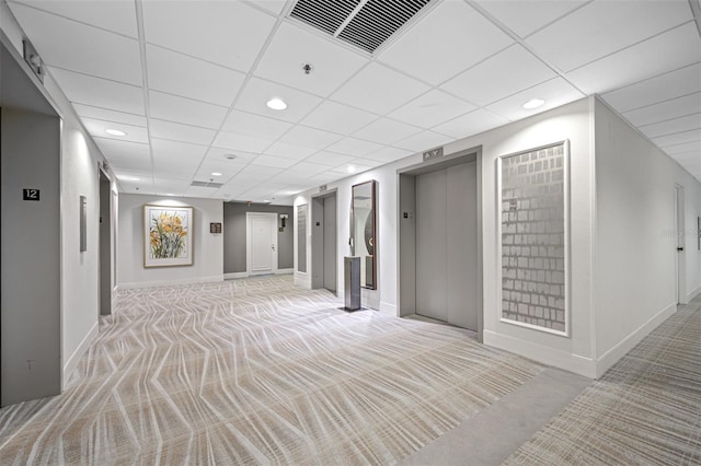 basement with light colored carpet, baseboards, a drop ceiling, visible vents, and elevator