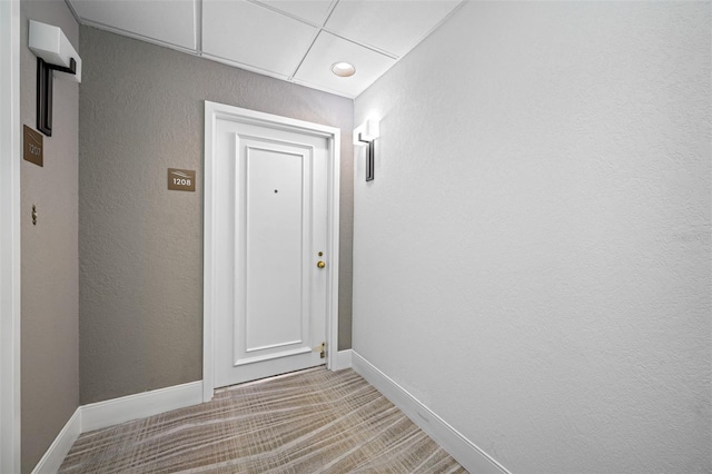 hall featuring carpet floors, a textured wall, and baseboards