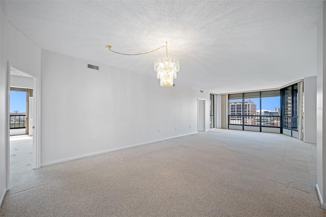 carpeted empty room featuring a textured ceiling, visible vents, baseboards, and a chandelier