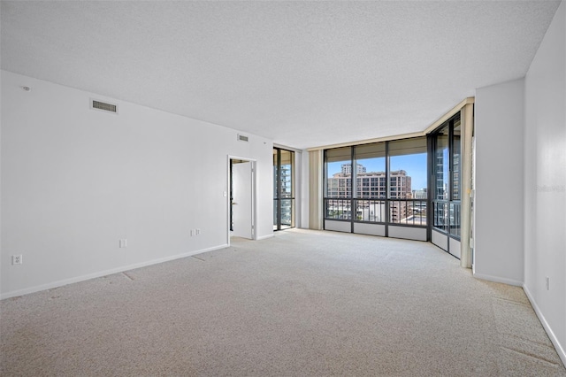 carpeted spare room featuring a textured ceiling, visible vents, baseboards, floor to ceiling windows, and a view of city