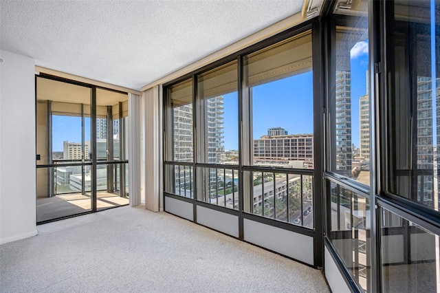unfurnished sunroom with baseboards, a textured ceiling, floor to ceiling windows, carpet floors, and a city view