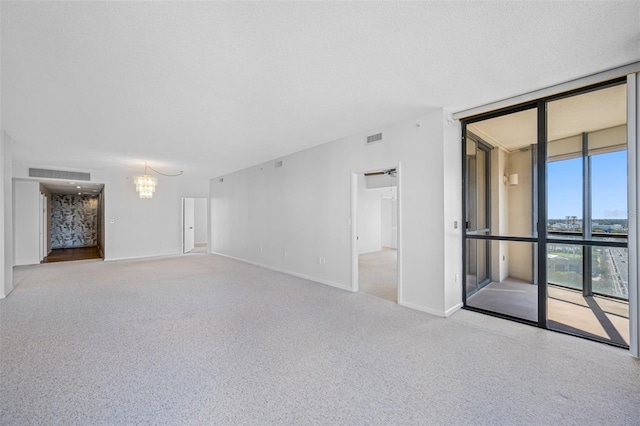 empty room with a textured ceiling, visible vents, an inviting chandelier, and a wall of windows