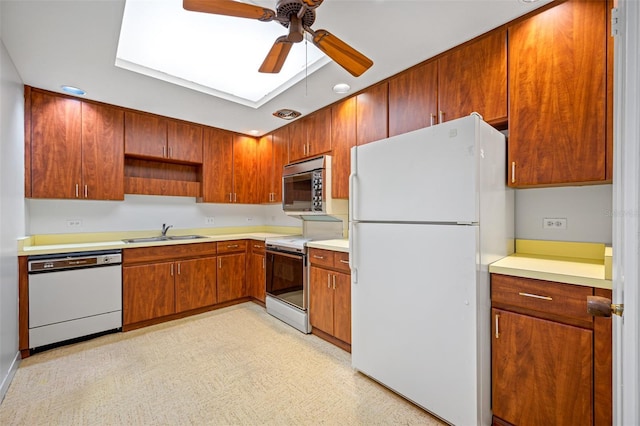 kitchen with light countertops, white appliances, a sink, a skylight, and a ceiling fan