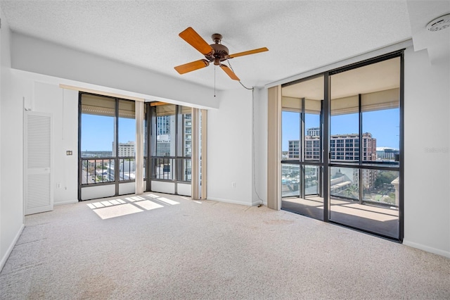 unfurnished room featuring a textured ceiling, a city view, ceiling fan, expansive windows, and carpet floors