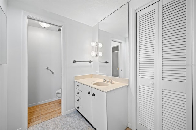 bathroom featuring baseboards, a closet, toilet, and vanity