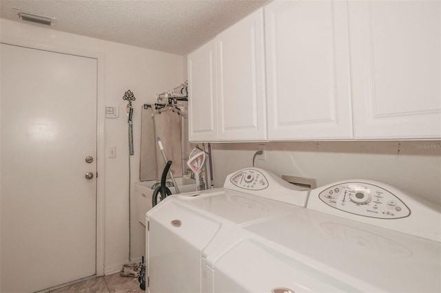 laundry area with cabinets, washing machine and clothes dryer, a textured ceiling, and light tile patterned flooring