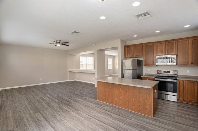 kitchen featuring ceiling fan, a kitchen island, a textured ceiling, dark hardwood / wood-style floors, and stainless steel appliances