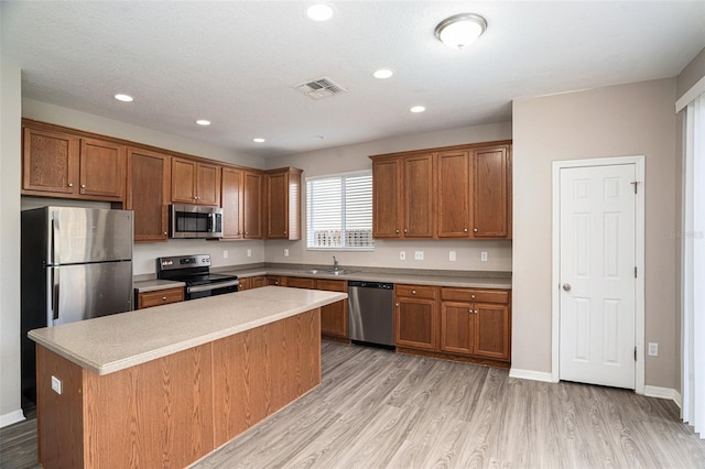 kitchen with a kitchen island, light hardwood / wood-style flooring, stainless steel appliances, sink, and a textured ceiling