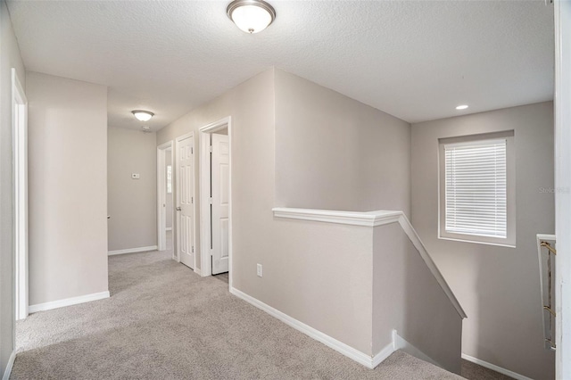 corridor with a textured ceiling and light colored carpet