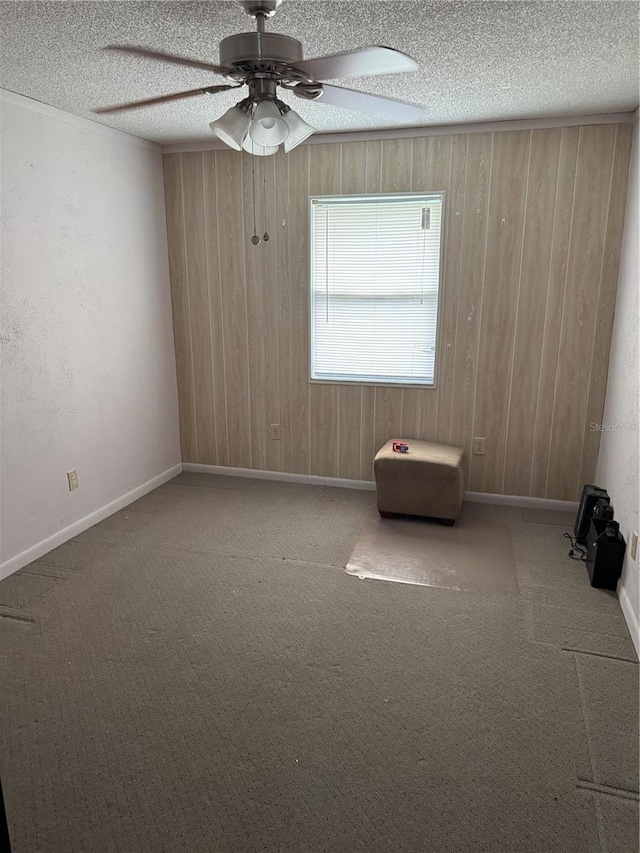 empty room featuring carpet, ceiling fan, wood walls, and a textured ceiling