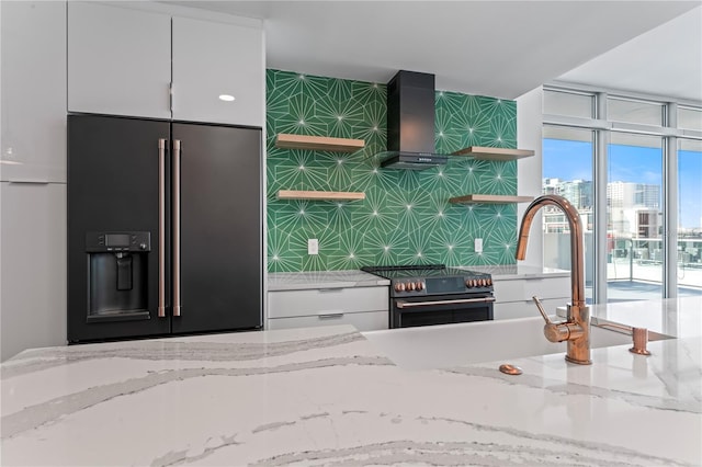 kitchen featuring light stone counters, white cabinets, sink, wall chimney range hood, and appliances with stainless steel finishes