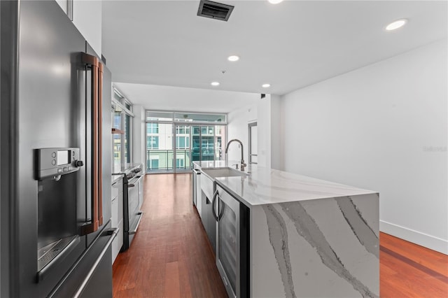 kitchen featuring wine cooler, light stone counters, stainless steel appliances, a center island with sink, and dark hardwood / wood-style floors