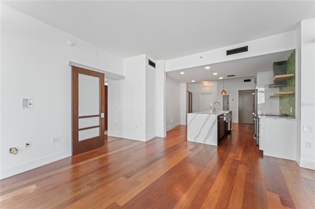 kitchen featuring a center island with sink, sink, hanging light fixtures, and dark hardwood / wood-style flooring