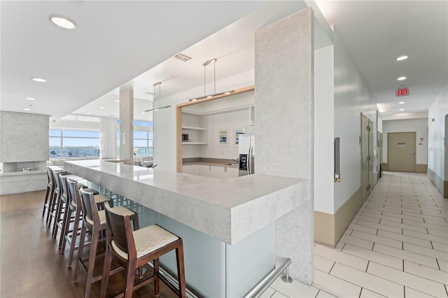 kitchen featuring a breakfast bar, white cabinetry, kitchen peninsula, decorative light fixtures, and stainless steel fridge