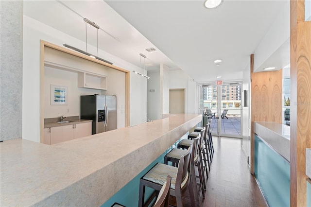 kitchen featuring stainless steel fridge, white cabinetry, a breakfast bar, dark hardwood / wood-style flooring, and decorative light fixtures