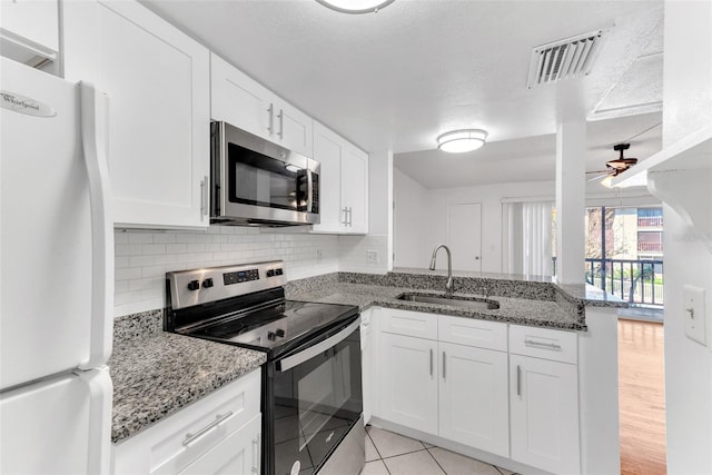 kitchen with kitchen peninsula, dark stone countertops, sink, white cabinets, and appliances with stainless steel finishes