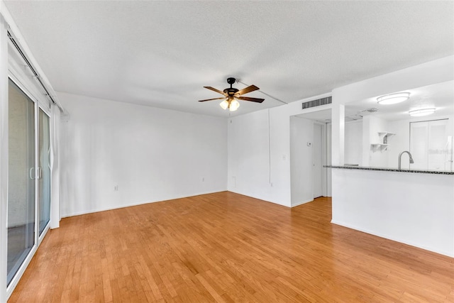 unfurnished living room with ceiling fan, a textured ceiling, and light wood-type flooring