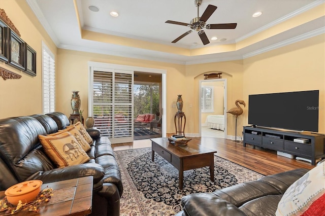 living room featuring wood-type flooring, ornamental molding, ceiling fan, and a tray ceiling