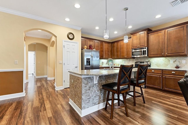 kitchen with pendant lighting, a center island with sink, appliances with stainless steel finishes, dark hardwood / wood-style flooring, and ornamental molding