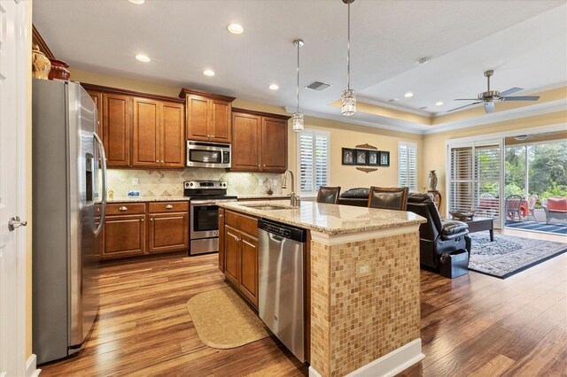 kitchen with wood-type flooring, sink, stainless steel appliances, a center island with sink, and decorative light fixtures