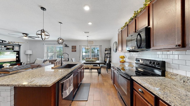 kitchen with light wood-type flooring, sink, an island with sink, black appliances, and ceiling fan