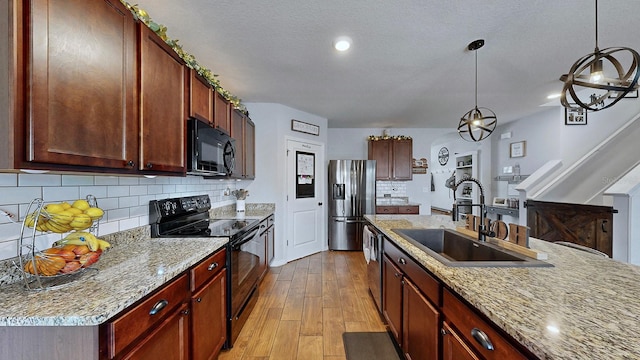 kitchen with a kitchen island with sink, sink, hanging light fixtures, light hardwood / wood-style flooring, and black appliances