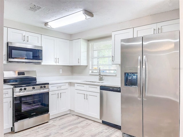 kitchen featuring appliances with stainless steel finishes, white cabinetry, light wood-type flooring, a textured ceiling, and sink