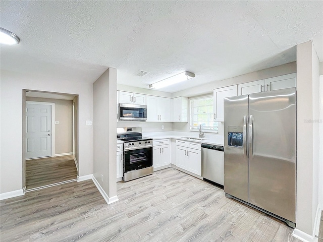 kitchen with light wood-type flooring, a textured ceiling, sink, white cabinetry, and appliances with stainless steel finishes