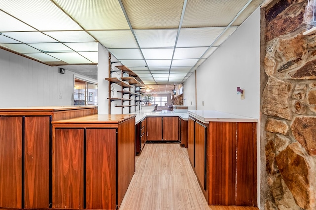 kitchen with kitchen peninsula, light hardwood / wood-style flooring, and a drop ceiling