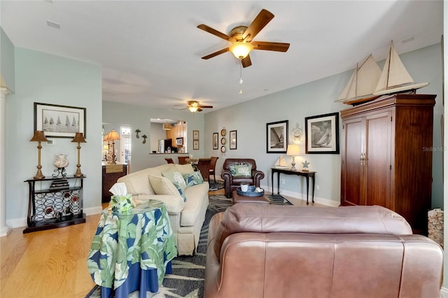 living room with light hardwood / wood-style floors, ceiling fan, and decorative columns