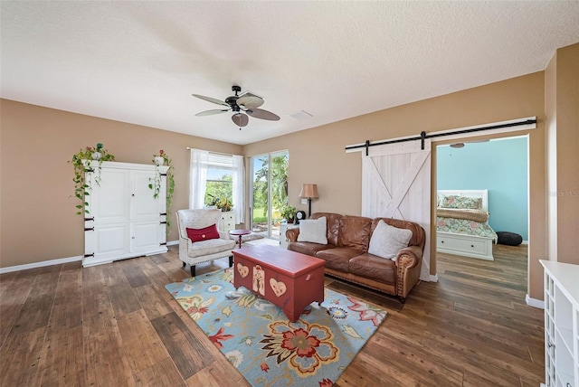 living room with ceiling fan, a textured ceiling, dark wood-type flooring, and a barn door