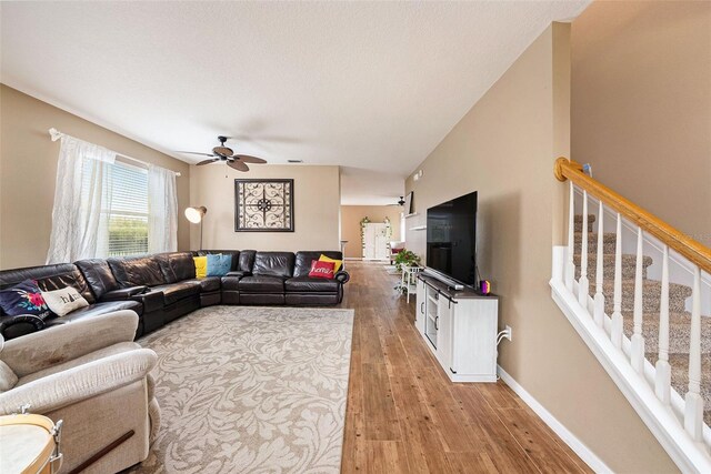 living room featuring light wood-type flooring, lofted ceiling, ceiling fan, and a textured ceiling