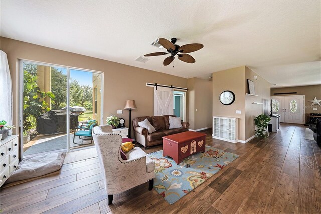 living room with a textured ceiling, ceiling fan, dark hardwood / wood-style floors, and a barn door