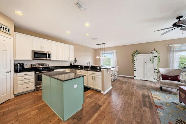 kitchen with appliances with stainless steel finishes, hanging light fixtures, kitchen peninsula, dark hardwood / wood-style flooring, and ceiling fan