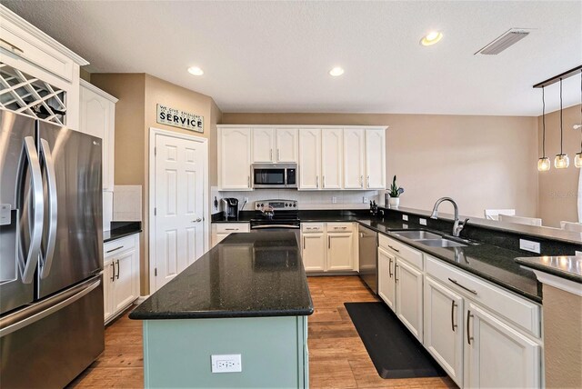 kitchen with sink, light hardwood / wood-style flooring, appliances with stainless steel finishes, decorative light fixtures, and dark stone countertops