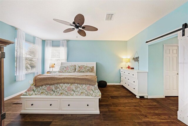 bedroom featuring a barn door, dark hardwood / wood-style flooring, and ceiling fan