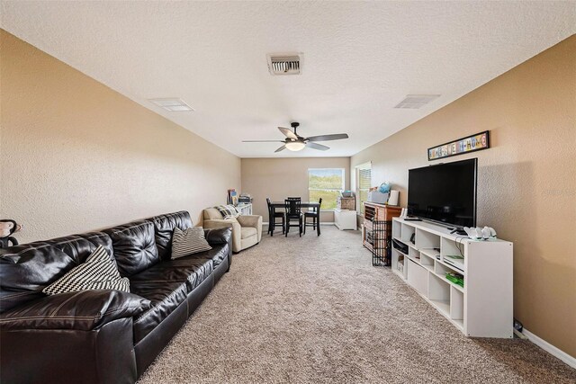 carpeted living room featuring ceiling fan and a textured ceiling