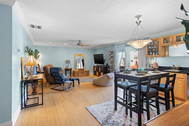 dining space featuring ceiling fan, sink, a textured ceiling, crown molding, and light hardwood / wood-style floors