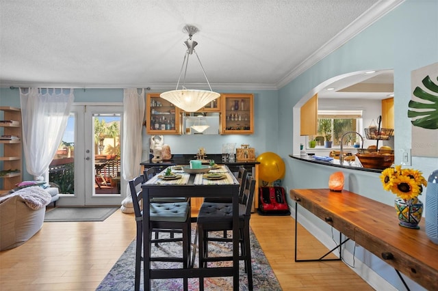 dining area with light wood-type flooring, a textured ceiling, and ornamental molding