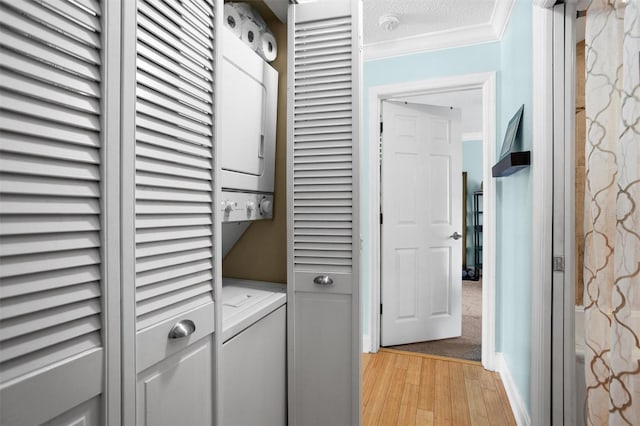 laundry area featuring a textured ceiling, light hardwood / wood-style flooring, stacked washer / dryer, and crown molding