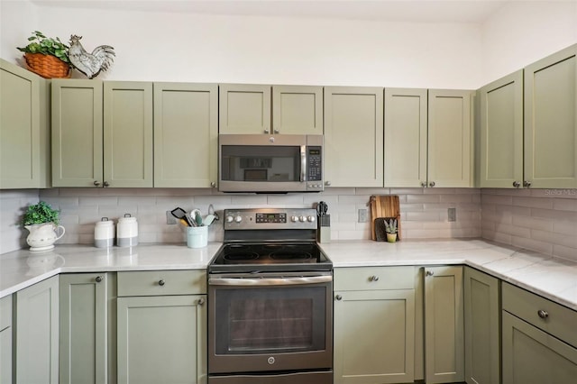 kitchen with light stone counters, appliances with stainless steel finishes, green cabinets, and decorative backsplash