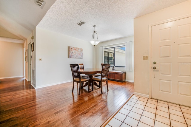 dining area with a textured ceiling, light wood-type flooring, and vaulted ceiling