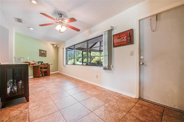 spare room with a textured ceiling, built in desk, light tile patterned floors, and ceiling fan