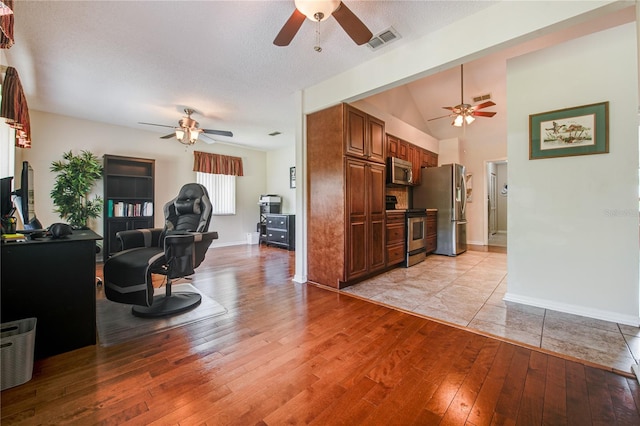 living room featuring light hardwood / wood-style floors, a textured ceiling, ceiling fan, and vaulted ceiling