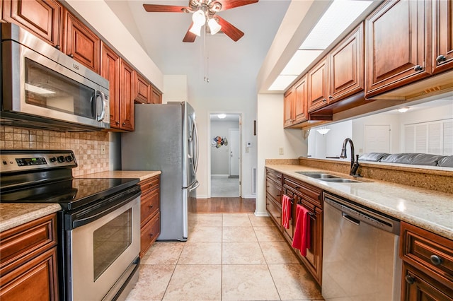 kitchen with light stone counters, vaulted ceiling, light tile patterned flooring, sink, and stainless steel appliances